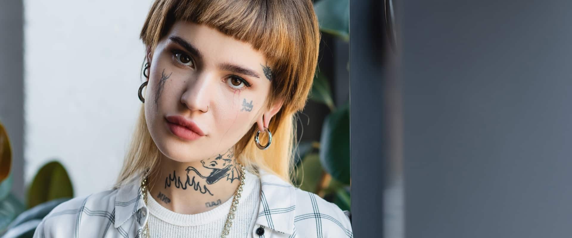 young and stylish woman with tattoo and piercing looking at camera in office, banner