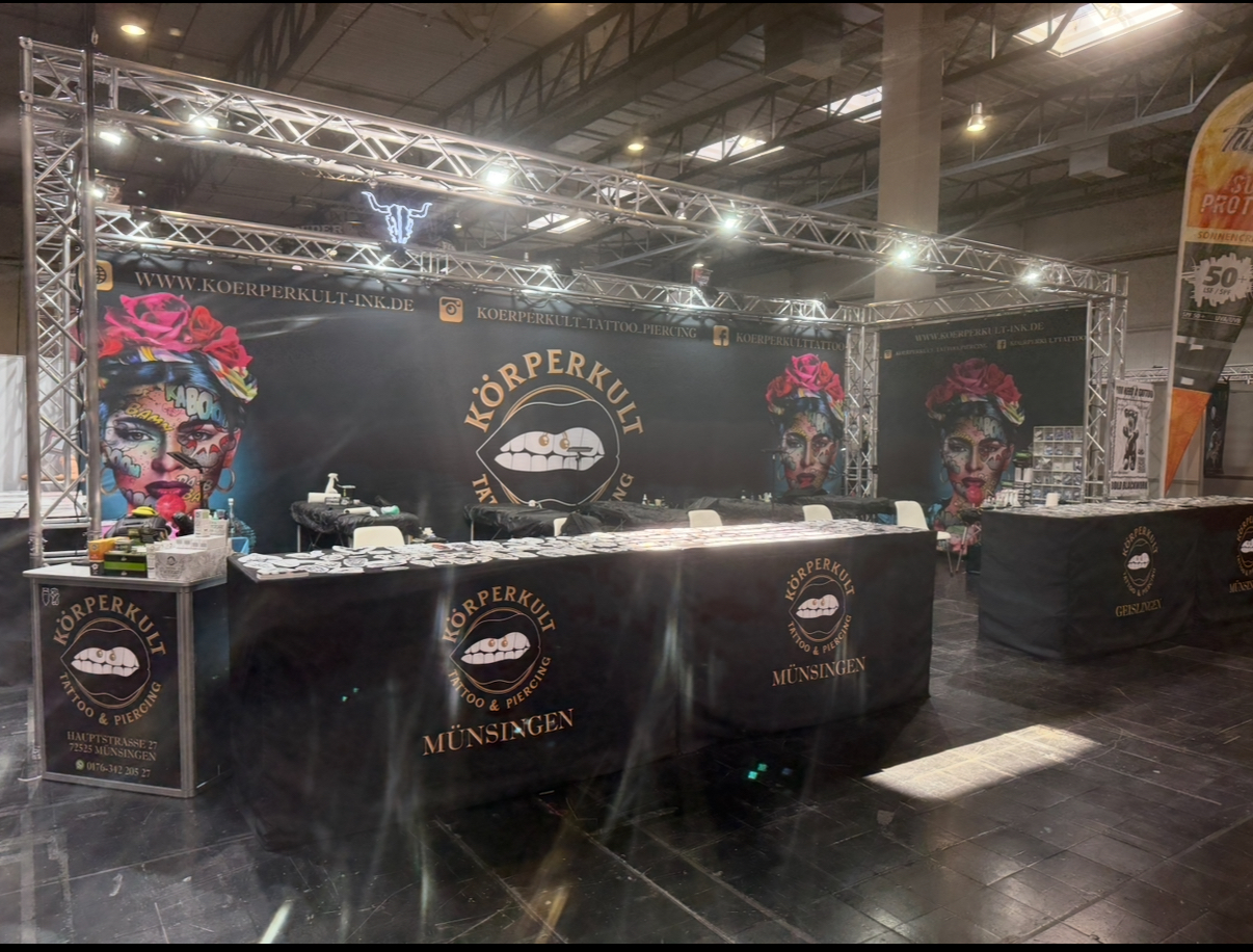 Messestand mit Kopfkunst-Logos, dekoriert mit farbenfrohen, kunstvollen Gesichtern und Blumen.