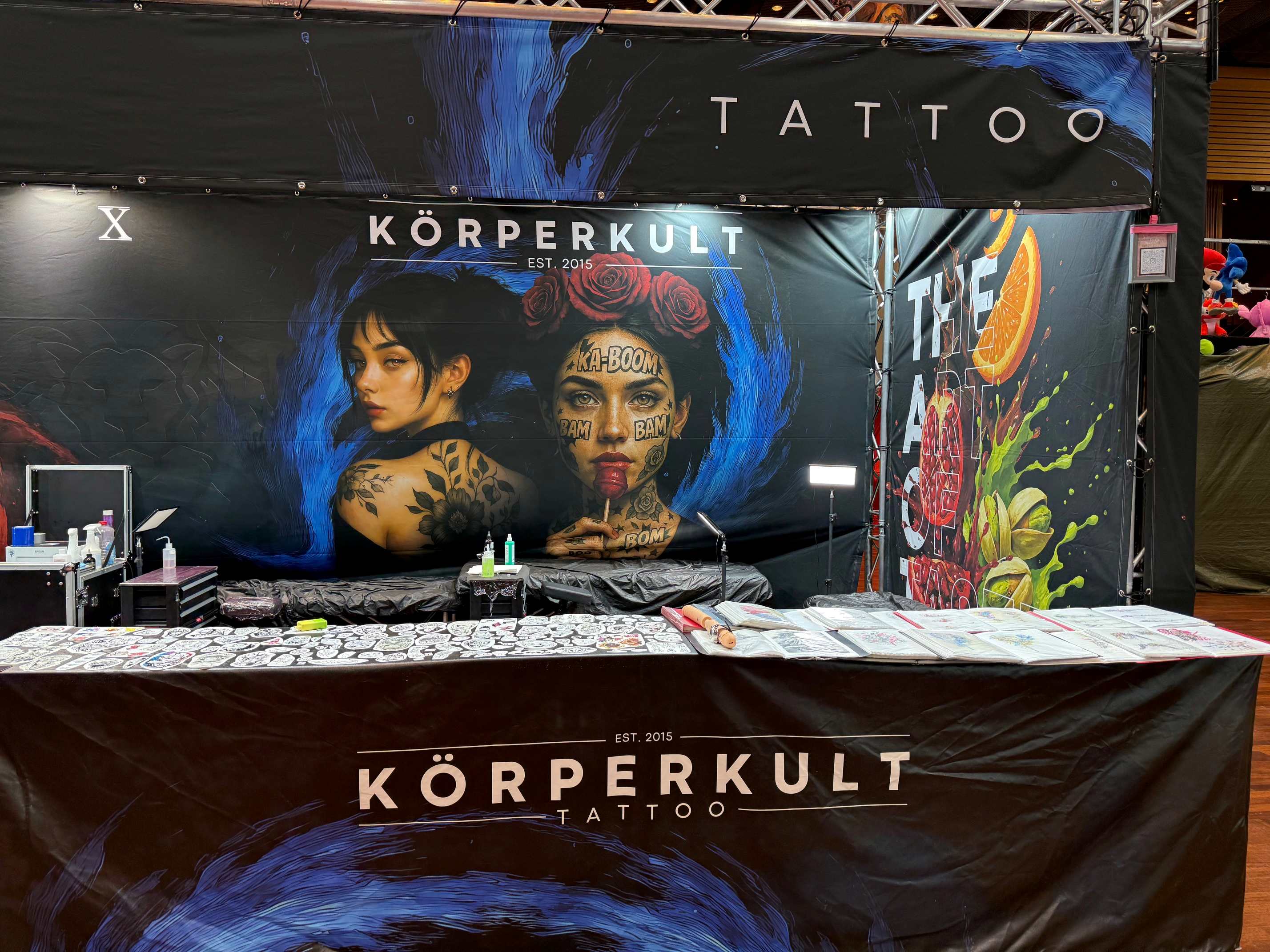 Ein Tattoo-Messestand mit grafischer Kunst; einladende, kreative Stimmung.