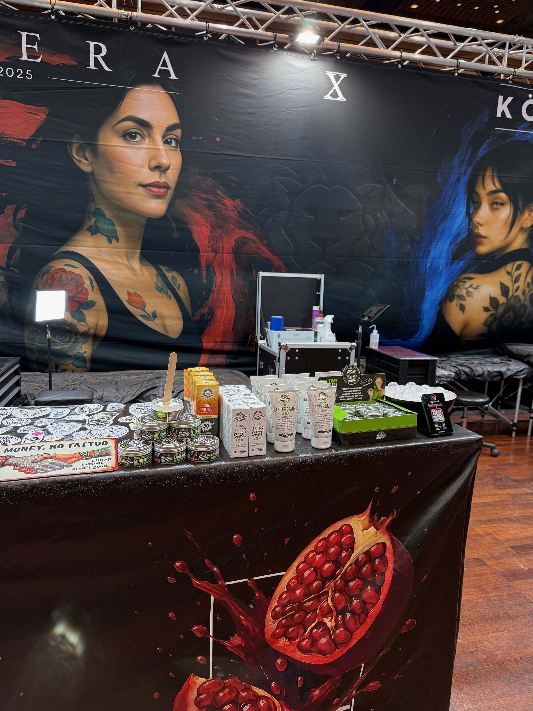 Eine Frau mit Tattoos schaut ernst; bunte Wandkunst im Hintergrund.
