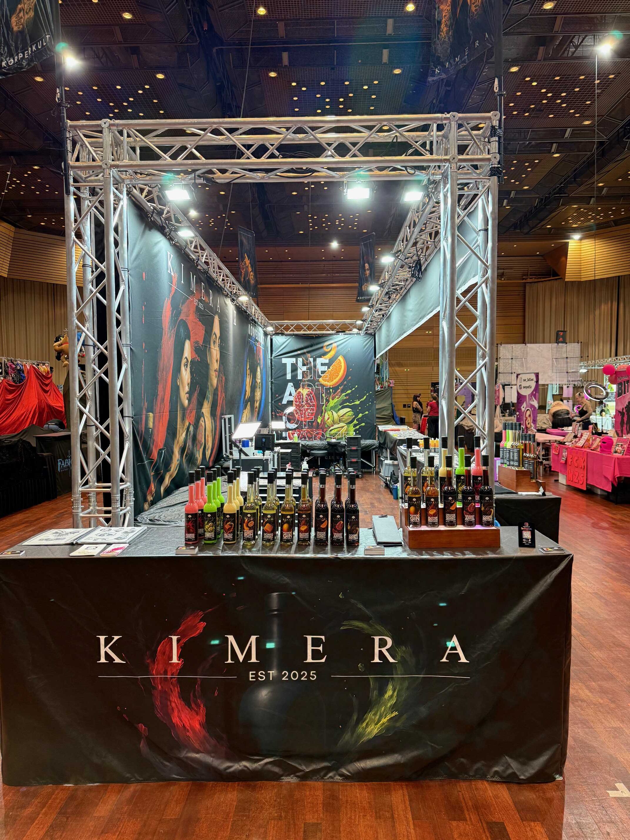 Ein Messestand mit bunten Flaschen, schwarzes Banner mit "KIMERA", Männergesicht.