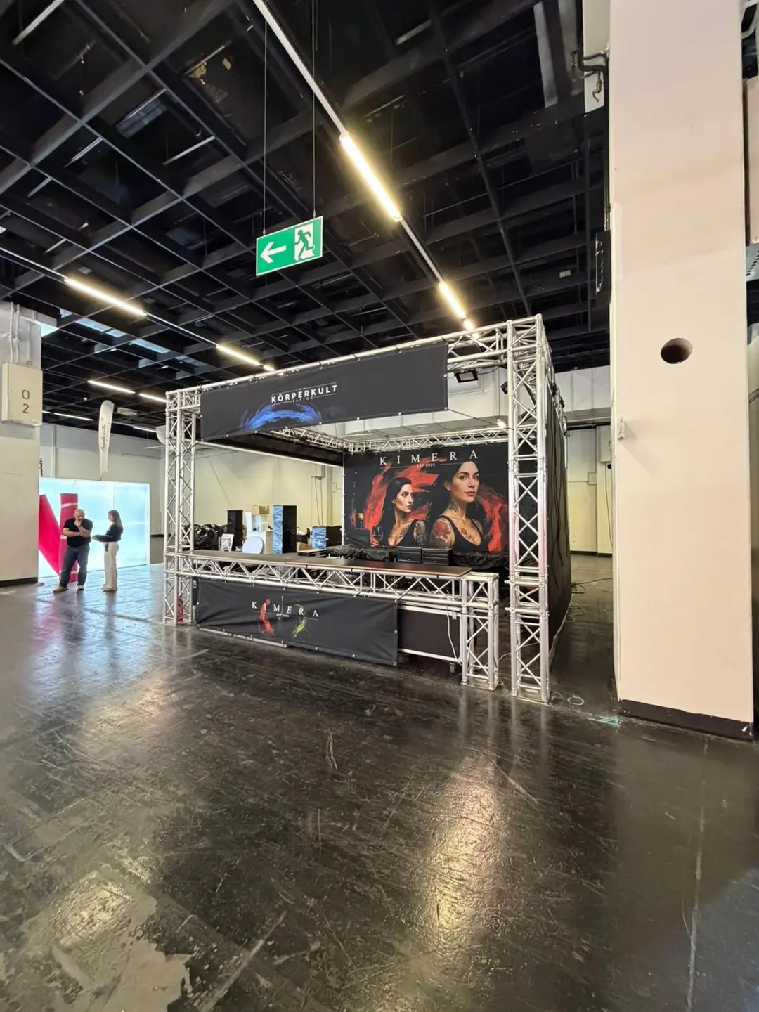 Messestand mit Kimera Plakat in schwarzer Halle zwei Personen unterhalten sich