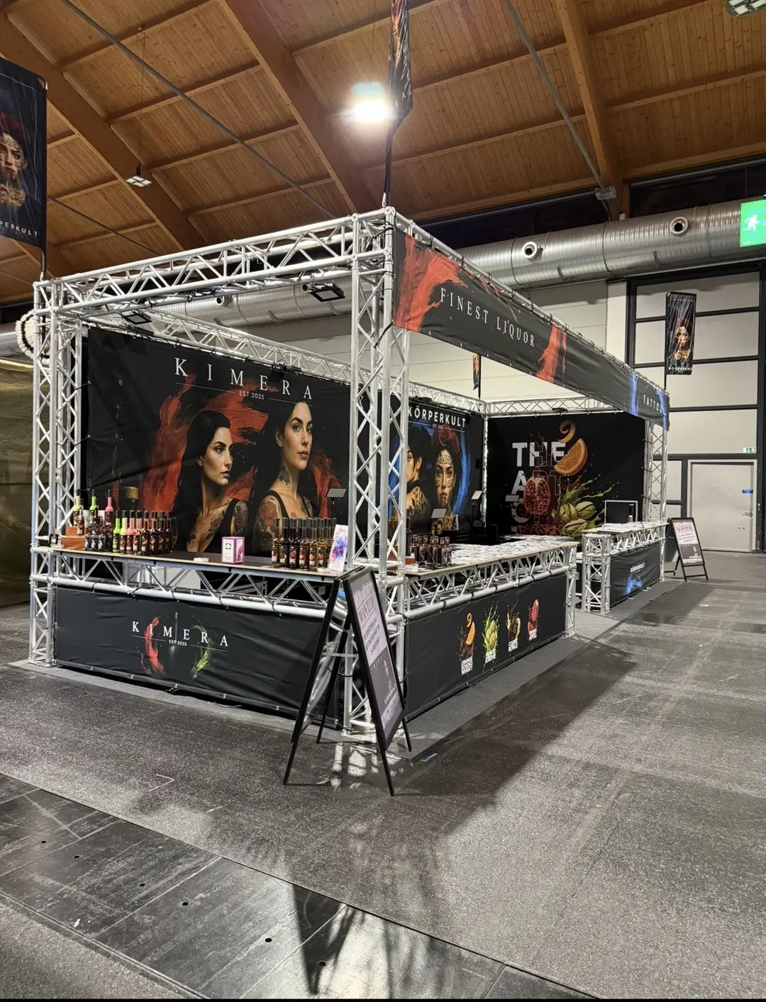 Messestand der Marke Kimera mit schwarzen Bannern und Spirituosenflaschen in einer Halle