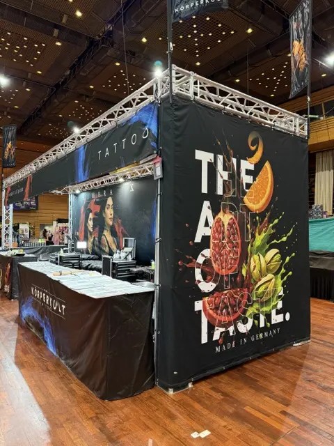 Schwarzer Messestand mit buntem Werbebanner und Tattoo Schriftzug in Halle