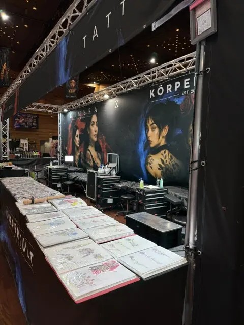 Tattoo Messestand mit grossen Postern und ausgelegten Designmappen auf dem Tisch